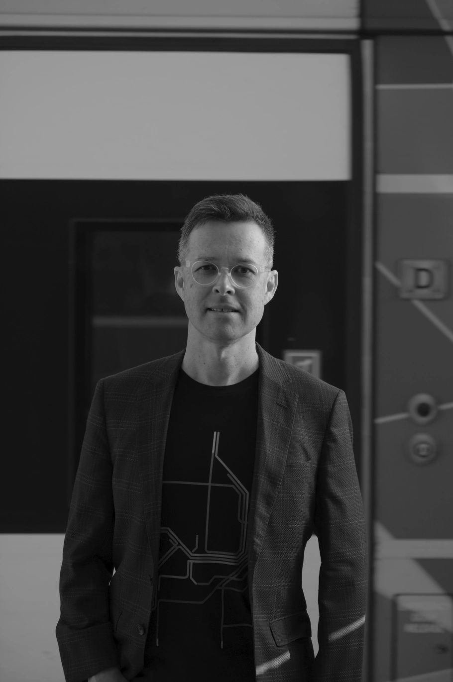Man with glasses wearing a blazer and black shirt.
