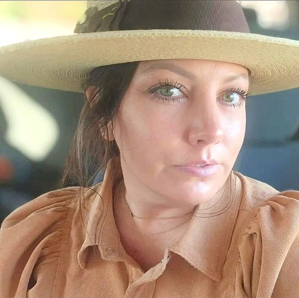Woman with green eyes wearing a beige hat and brown shirt.