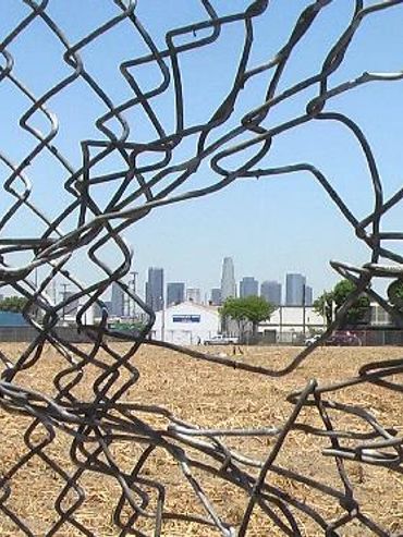 City view through broken chain-link fence.