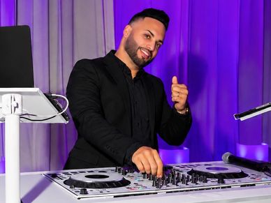 DJ smiling and giving a thumbs up behind a DJ console.