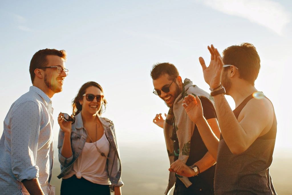 Four friends laughing and enjoying outdoors in bright sunlight.