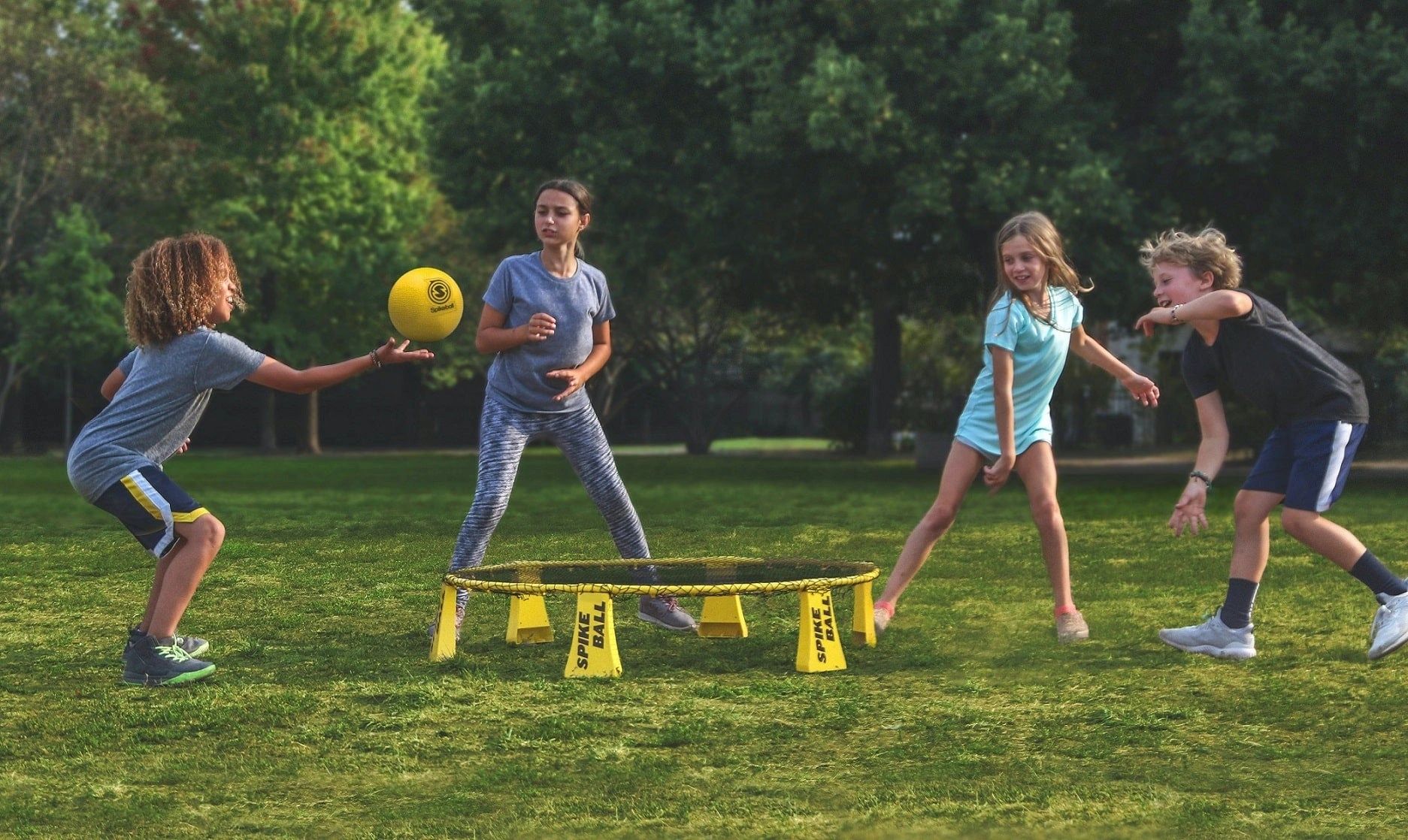 Children playing spikeball outdoors on grass.