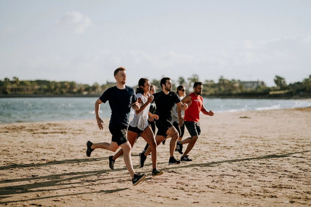Five people running on a beach near the water.
