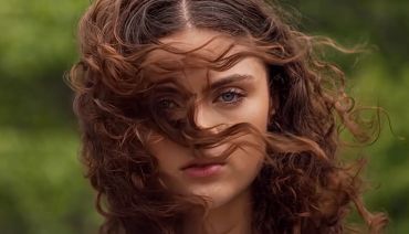 Close-up of a woman with curly hair blowing in the wind.
