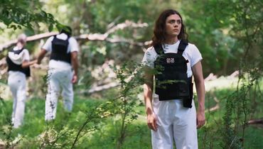 Three people wearing white pants and black vests in the forest.