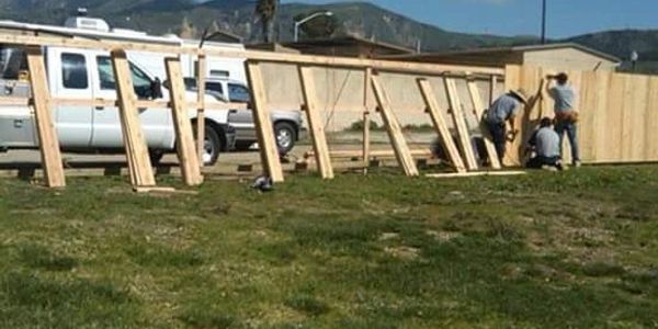 Workers assembling a wooden fence outside on a sunny day.
