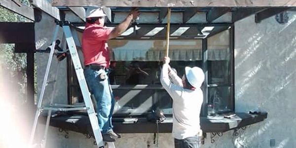 Two construction workers measuring a pergola beam outdoors.