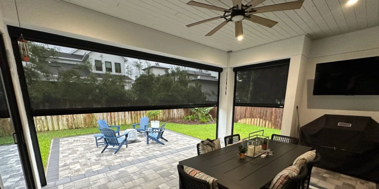 black exterior motorized privacy screen with black dining set and grey pavers and fire pit