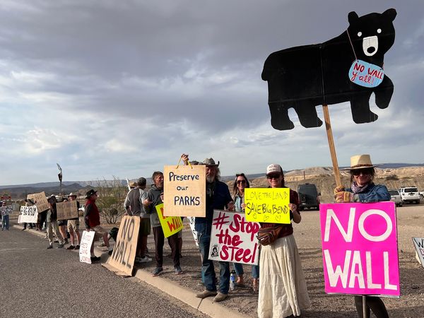 Protesters hold signs against building a border wall near a park.