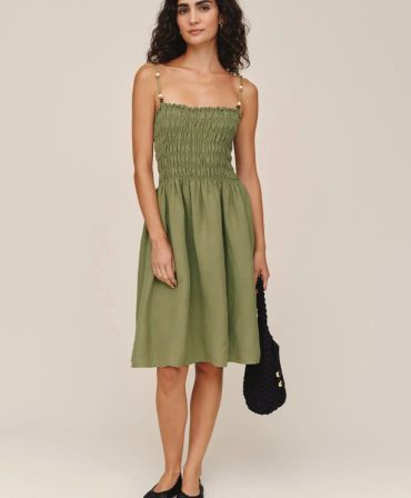 Woman in olive green smocked dress holding a black handbag.