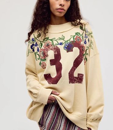 Woman wearing a beige sweatshirt with floral embroidery and the number 32.