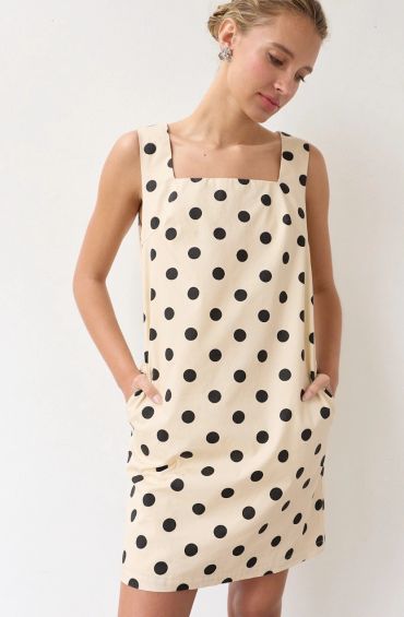 Woman wearing a beige dress with black polka dots and square neckline.
