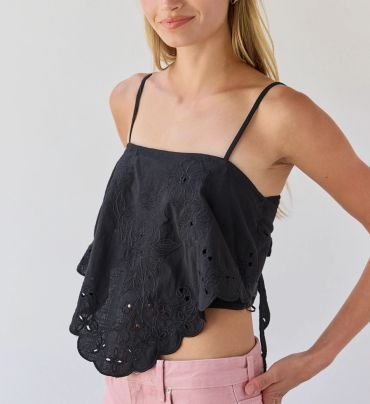 Woman wearing a black embroidered sleeveless top with pink pants.