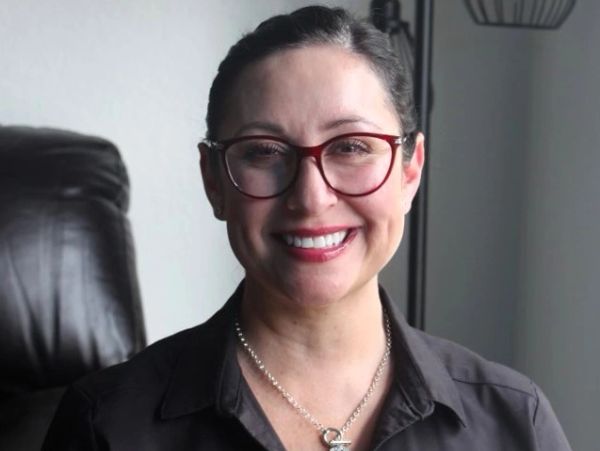 A smiling woman wearing glasses and a black shirt.