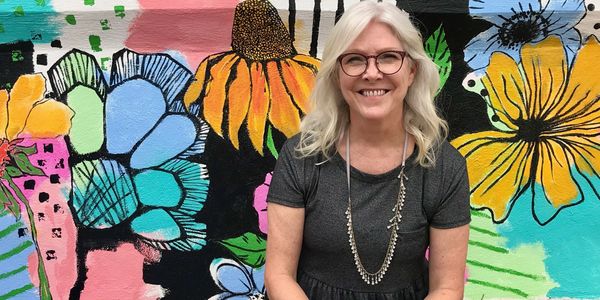 Beth Beck PhD in front of MillHouse mural at the McKinney Cotton Mill