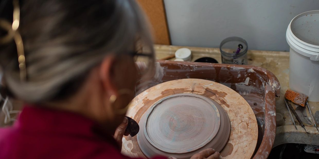 Person shaping a clay plate on a pottery wheel in a workshop.