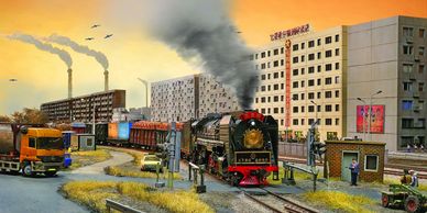 Model train scene with buildings, vehicles, and smoke.