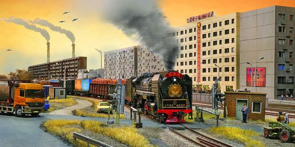 A steam locomotive emits smoke while passing through an urban area with factories and buildings.