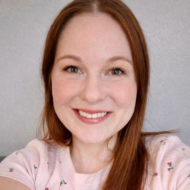 Smiling woman with red hair wearing a pink floral top.