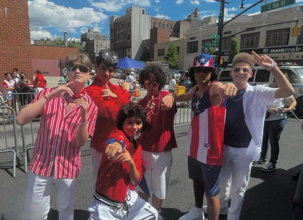A group of six young men posing confidently outdoors on a sunny day.