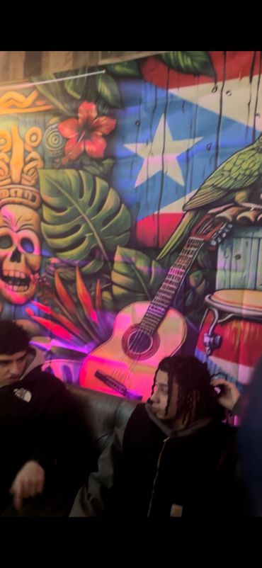 Two people sitting in front of a vibrant mural with tropical and musical themes.