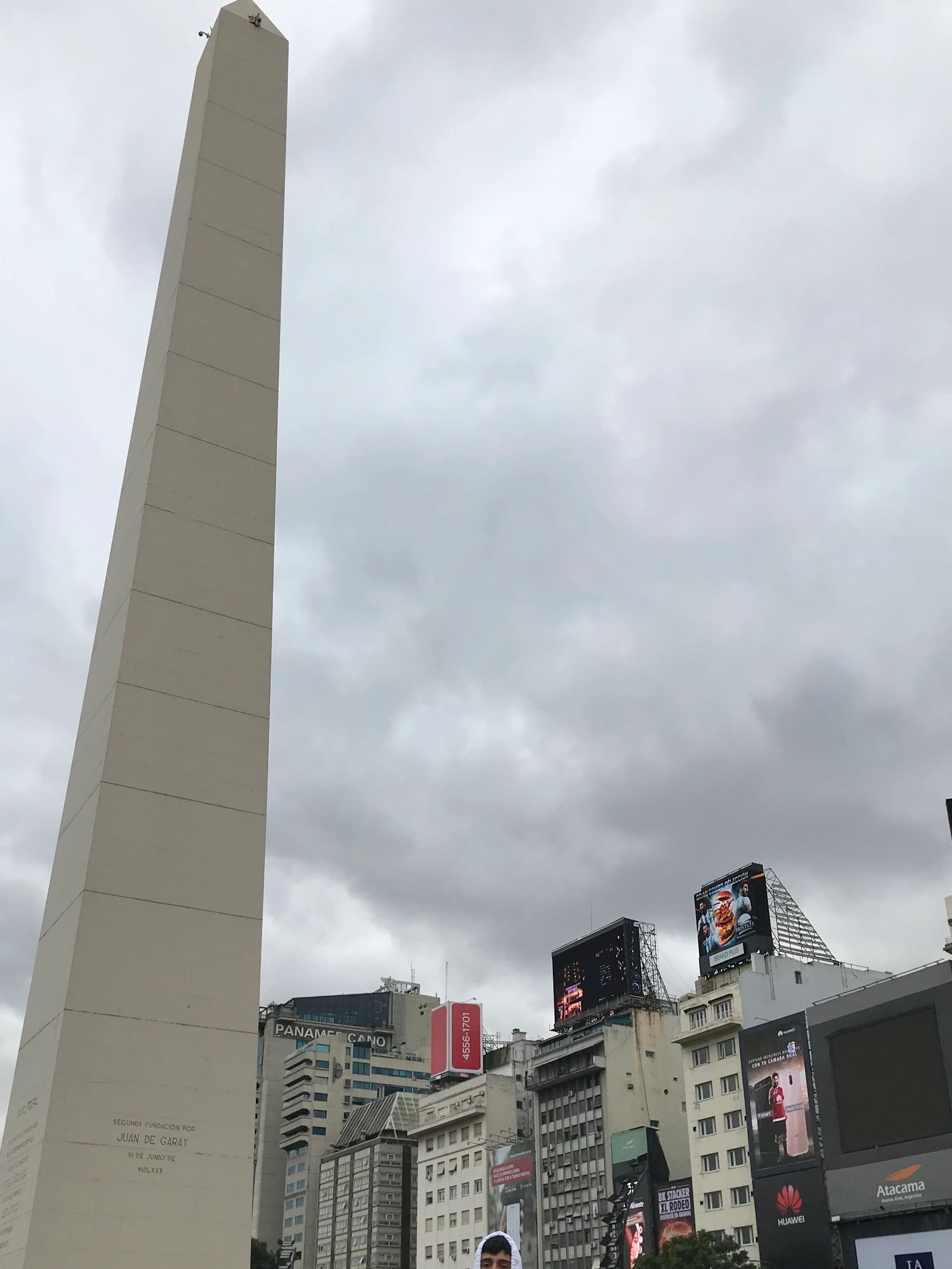 Obelisk in a busy urban square with people and cloudy sky.