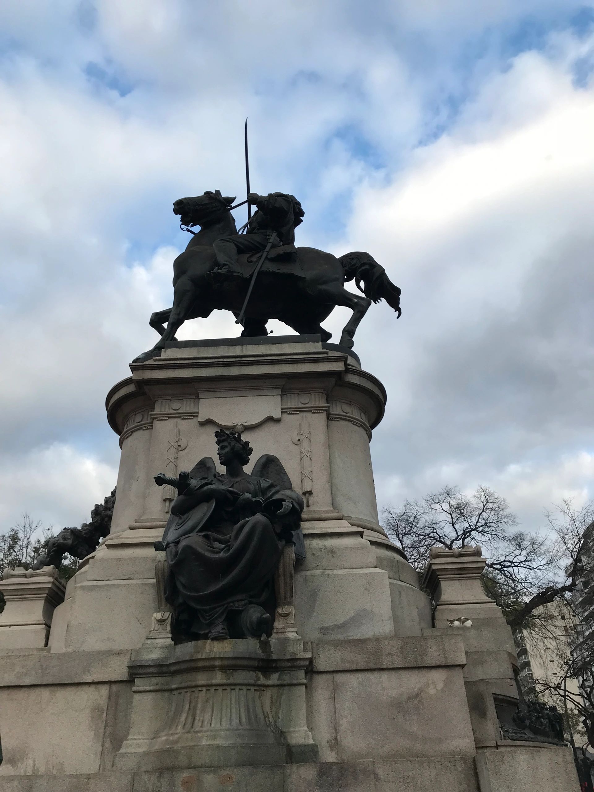 Equestrian statue atop a grand monument under cloudy sky.