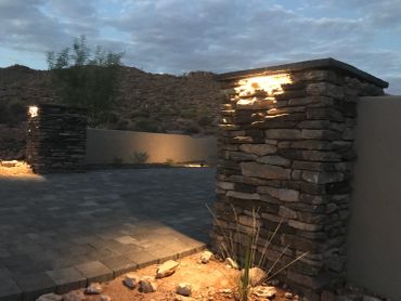 Stone pillars with lights illuminate a driveway at dusk.