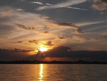 Sunset over calm water with clouds reflecting golden light.