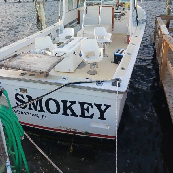 Fishing boat named SMOKEY docked at a marina with fishing chairs.