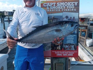Man holding a large fish in front of a fishing charter sign.