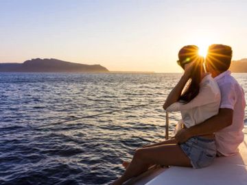 Couple embraces on a boat during a golden sunset over the ocean.