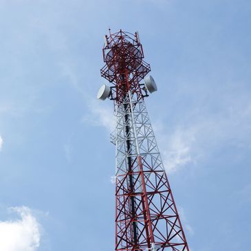 Tall red and white communication tower against blue sky.