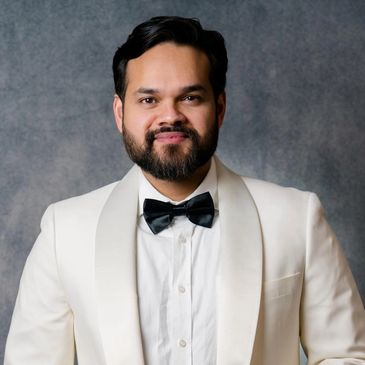 Man in white tuxedo with black bow tie smiling.