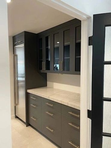 Dark kitchenette cabinets with glass-front uppers beside refrigerator