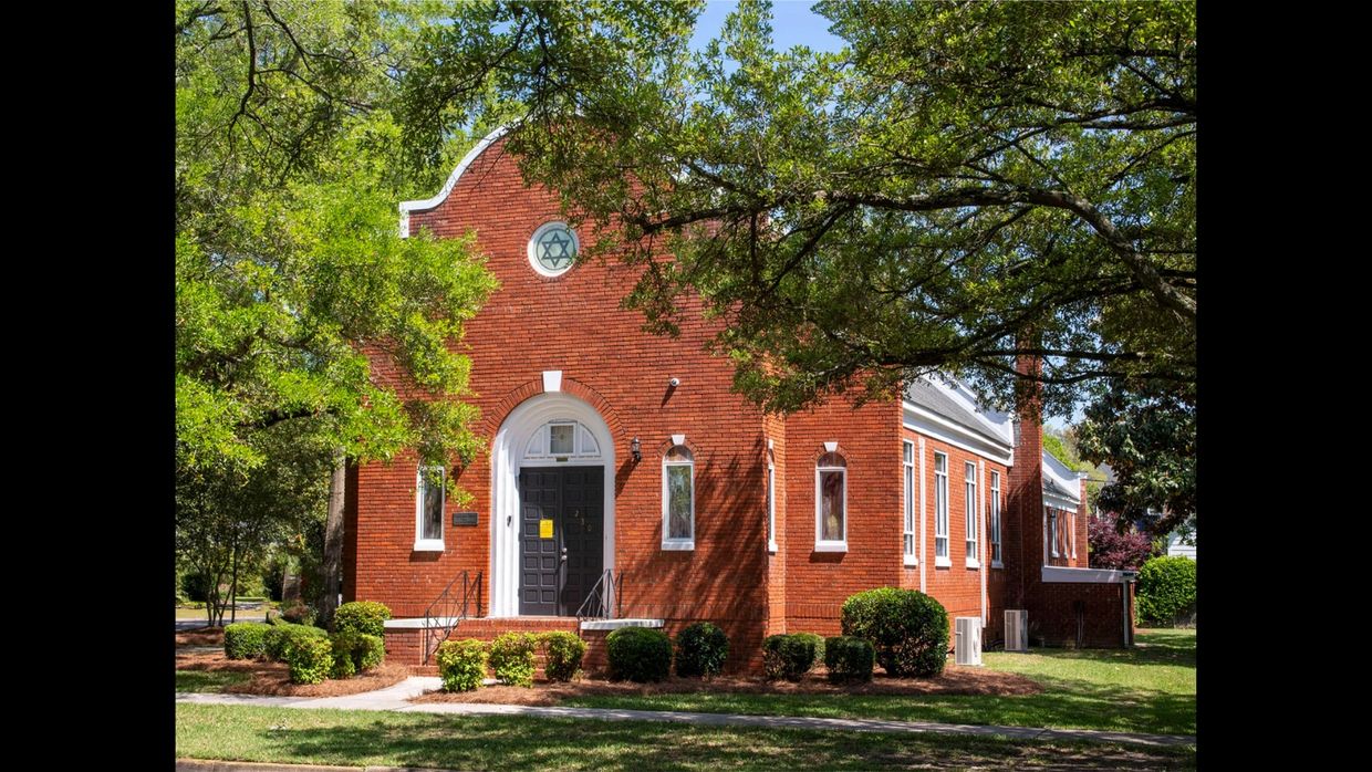 Red brick synagogue with a Star of David symbol above the entrance, surrounded by greenery.