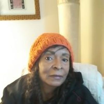 Woman wearing an orange knitted hat indoors.