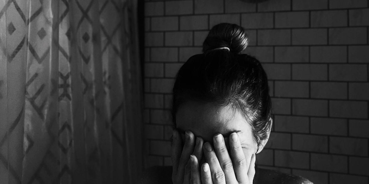 Woman covering her face with hands in black and white photo.