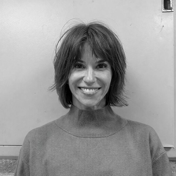 Smiling woman with short hair in a cozy sweater against a plain background.