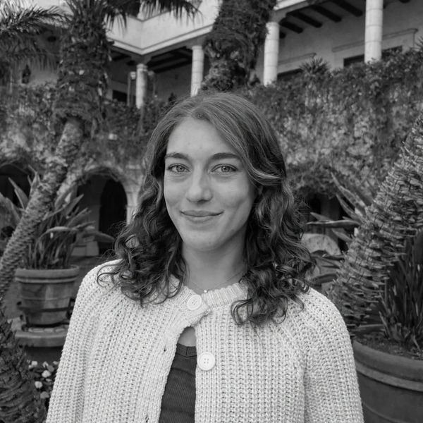 Young woman with curly hair smiling in a garden courtyard.