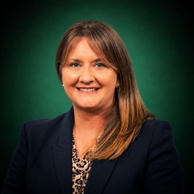 Smiling woman in a dark blazer with a green background.