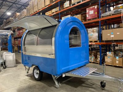 A blue food trailer with an open hatch in a warehouse.