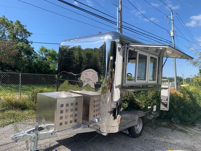 A shiny, metallic food trailer with an open serving window parked outdoors.