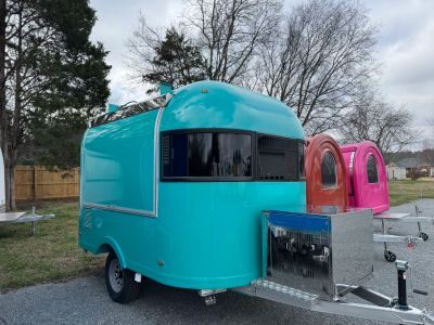 A small turquoise camper trailer parked outdoors with other colorful trailers.