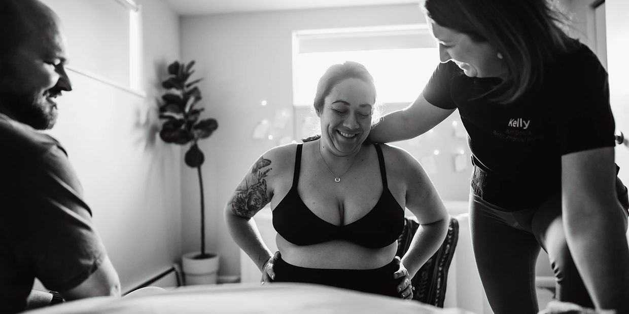Pregnant woman smiling with support from two people in a bright room.
