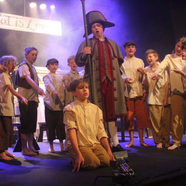 A boy sits on his knees, surrounded by orphans.  Production of Oliver.