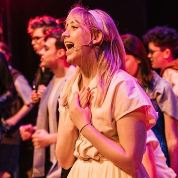 A young woman sings during the production of Grease.