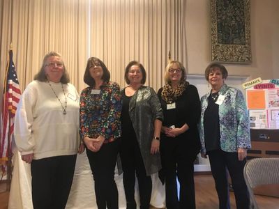 Group of five women standing indoors near an American flag.