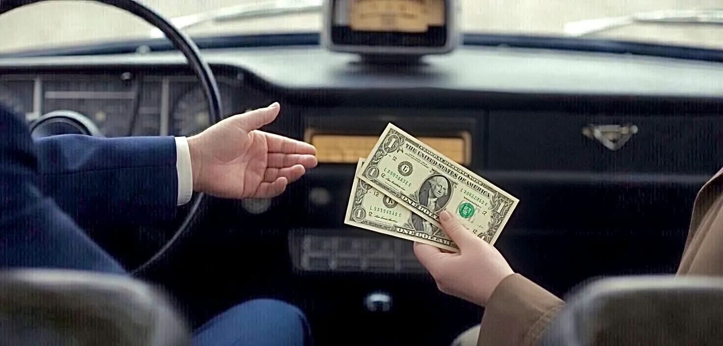 Person handing over dollar bills inside a car.