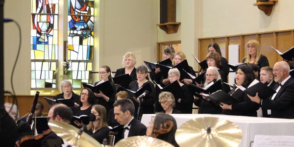 Choir performing in a church beneath stained glass windows.